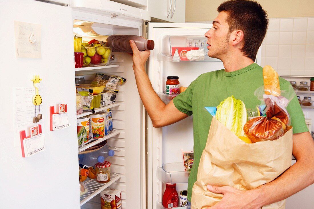 Young man storing food in refrigerator