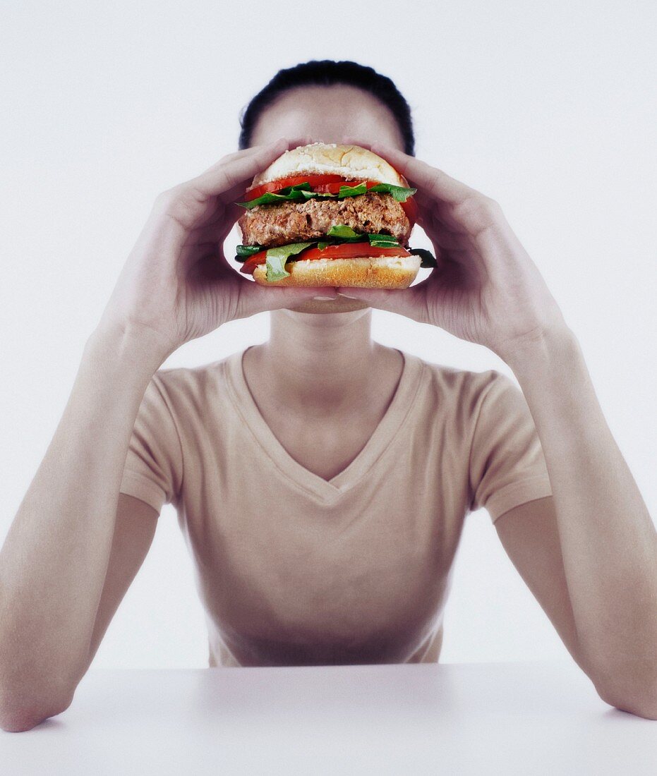 Young woman holding burger in front of face