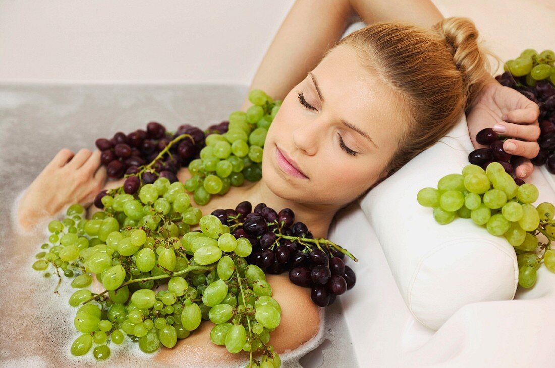 Young woman in bath with grapes