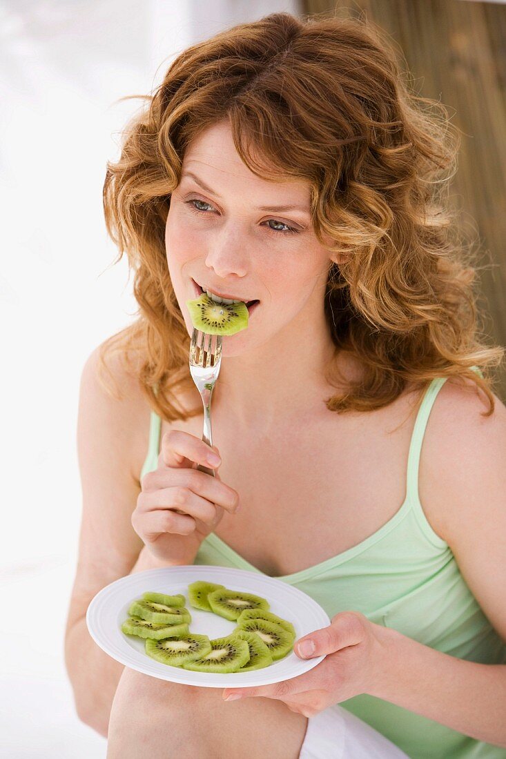 Young woman biting into a slice of kiwi fruit