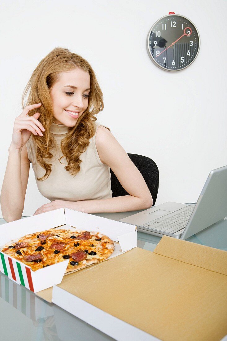 Junge Geschäftsfrau isst Pizza während der Mittagspause