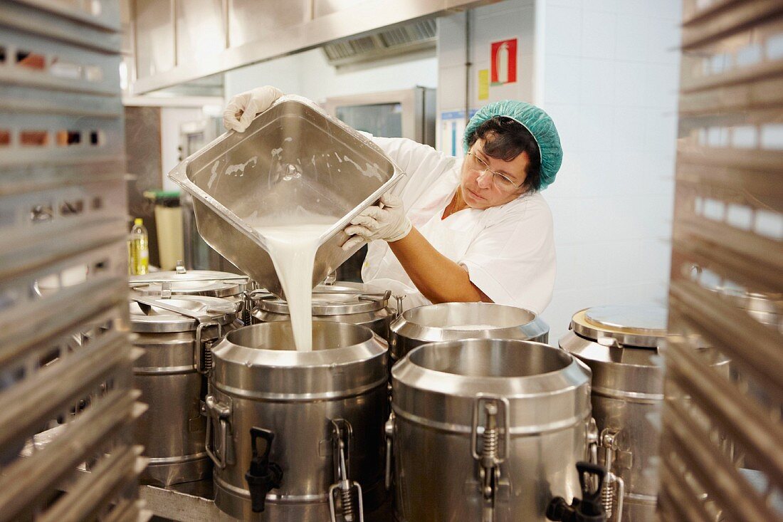 Eine Frau gießt in einer Großküche Milch in einen Behälter ein