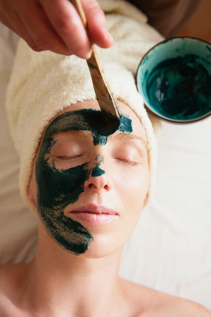 Green mud being applied to a woman's face