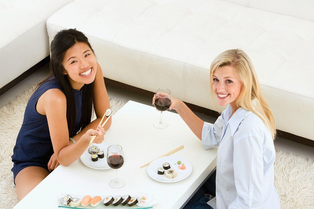 Two young women eating sushi in living room