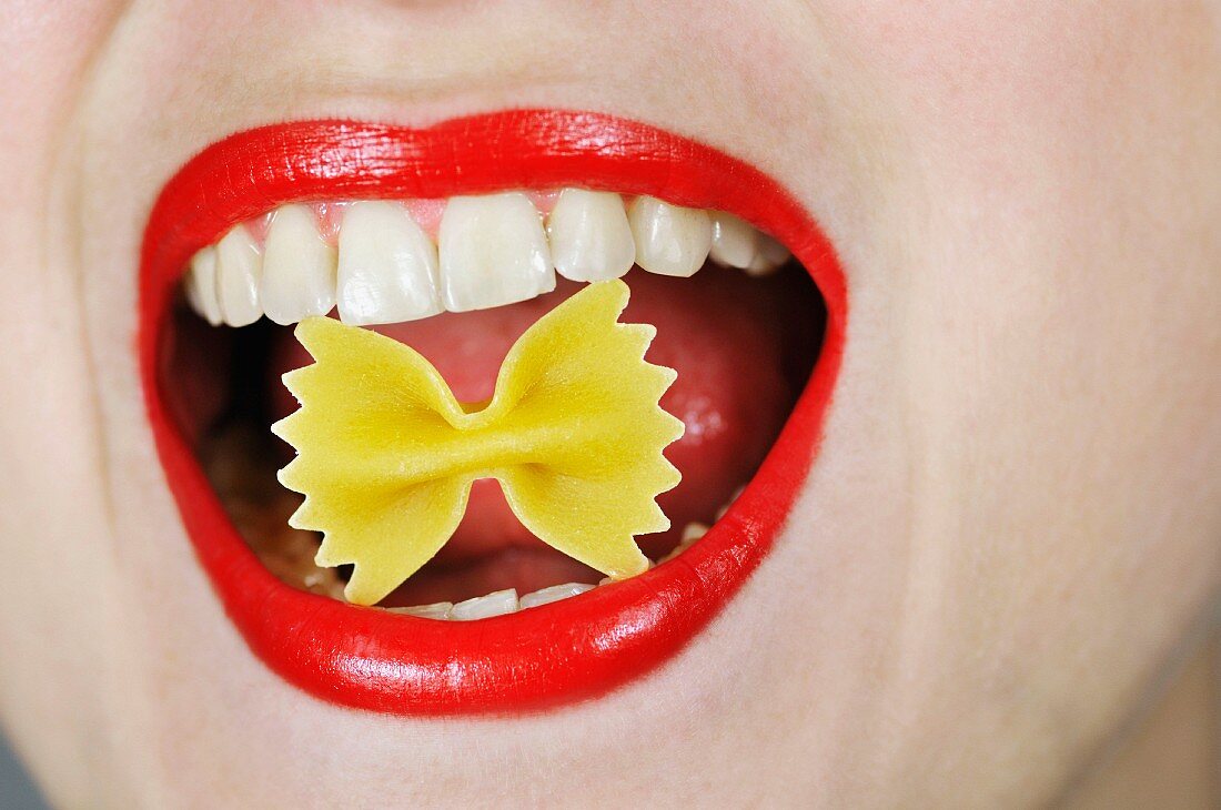 Woman with uncooked farfalle in her mouth