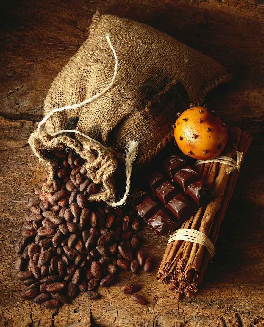 Jutesack mit Kakaobohnen, eine Tafel Schokolade, Zimtstangen und mit Nelken gespickte Orange