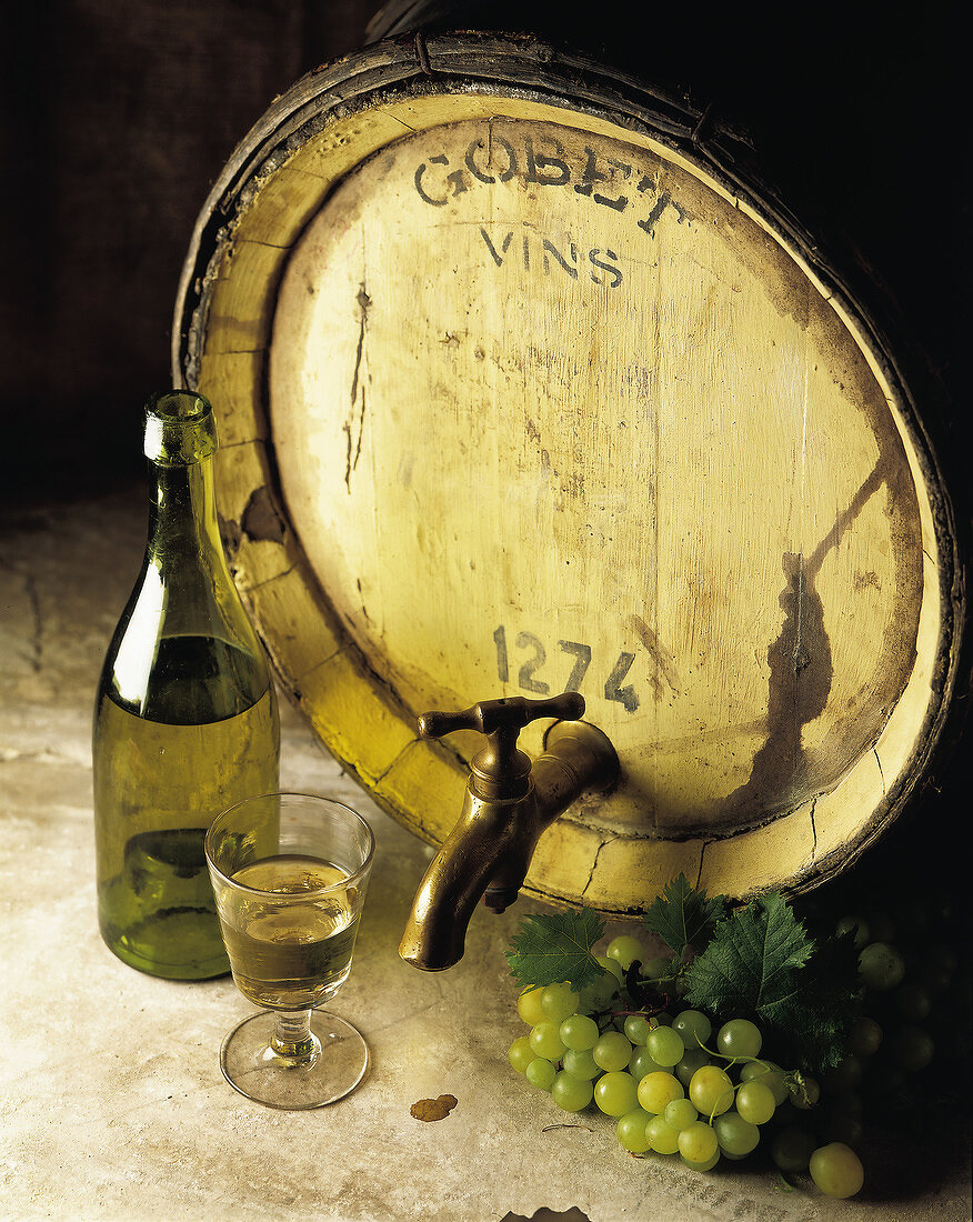 Ein Holzfass Weißwein mit Flasche, Glas und Weintrauben