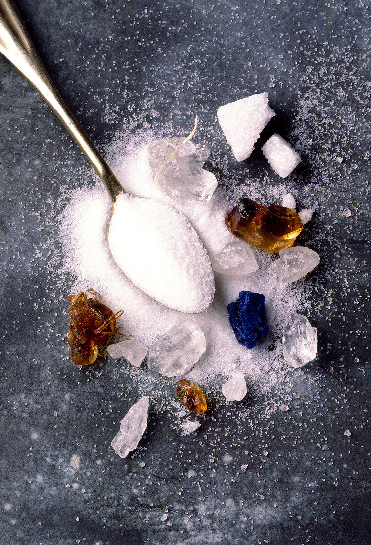 Verschiedene Zuckersorten mit Löffel auf grauem Untergrund
