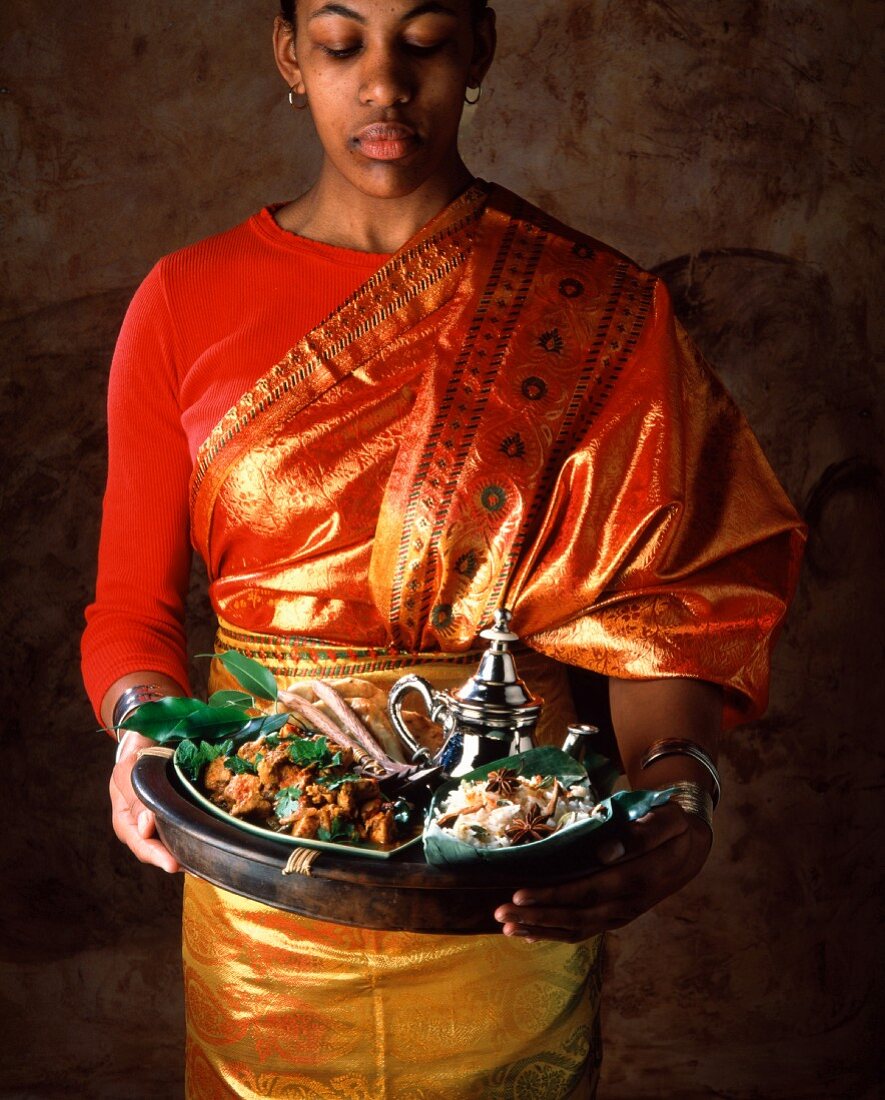 Indische Frau hält ein Tablett mit Basmati-Gewürzreis und Lammcurry