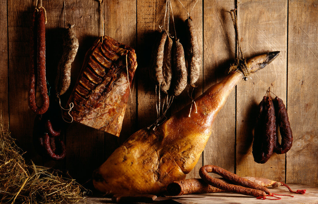 Verschiedene Schinken- und Wurstwaren an einer Holzwand hängend