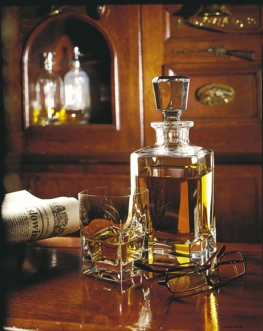 Whisky-Karaffe und Glas mit Zeitung und Brille im gemütlichen holzvertäfelten Raum