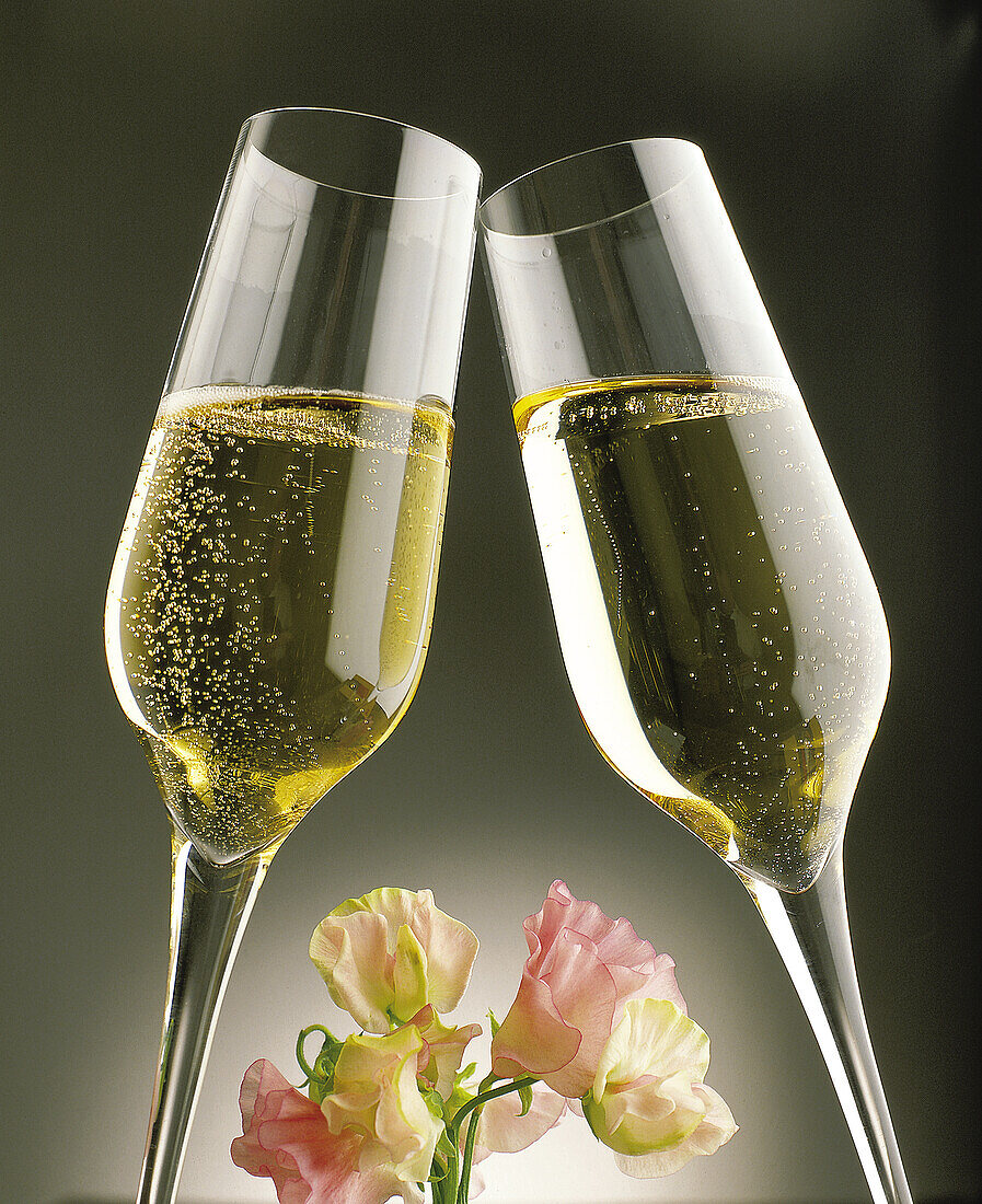 Zwei anstossende Champagnergläser mit pastellfarbenen Blüten