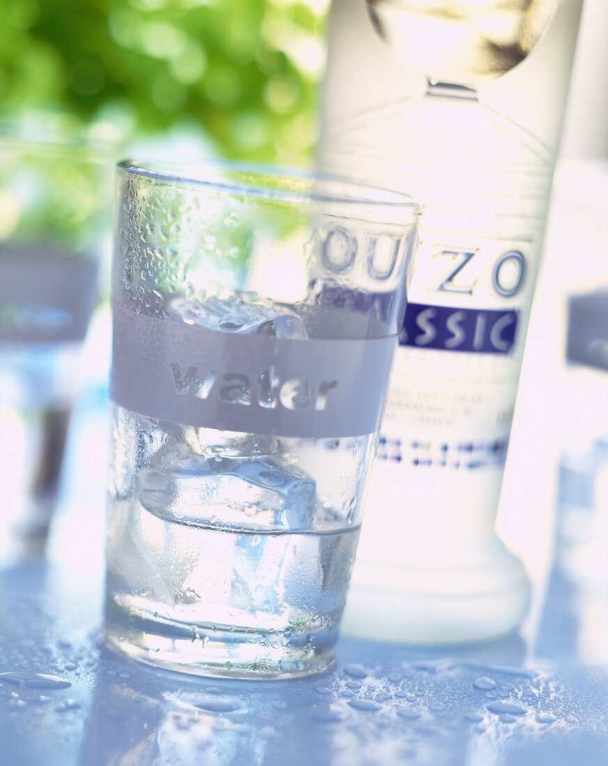 Eine Flasche Ouzo und ein Glas Wasser mit Eiswürfeln