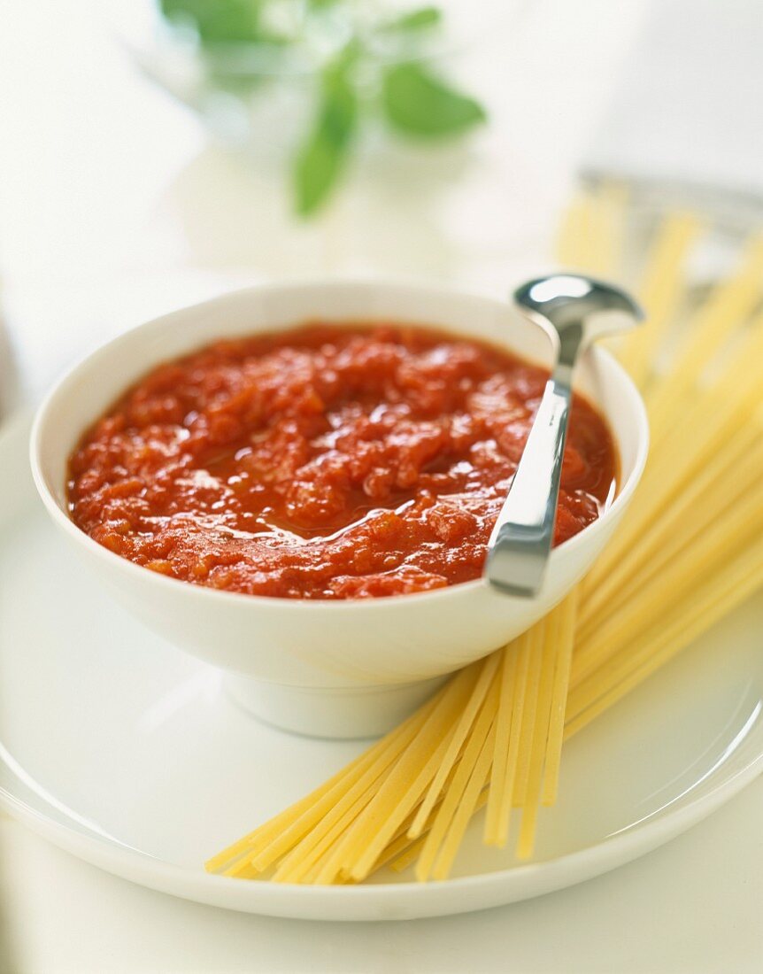 Tomatensauce in einem Schälchen, daneben ungekochte Spaghetti