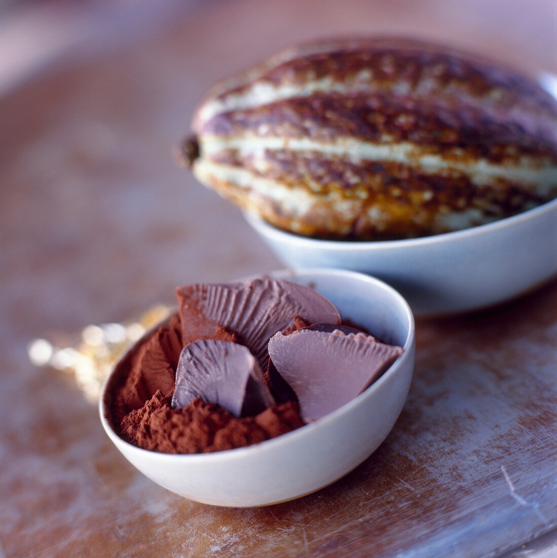 Kakaopulver mit Schokolade in einem Schälchen, dahinter Kakaofrucht