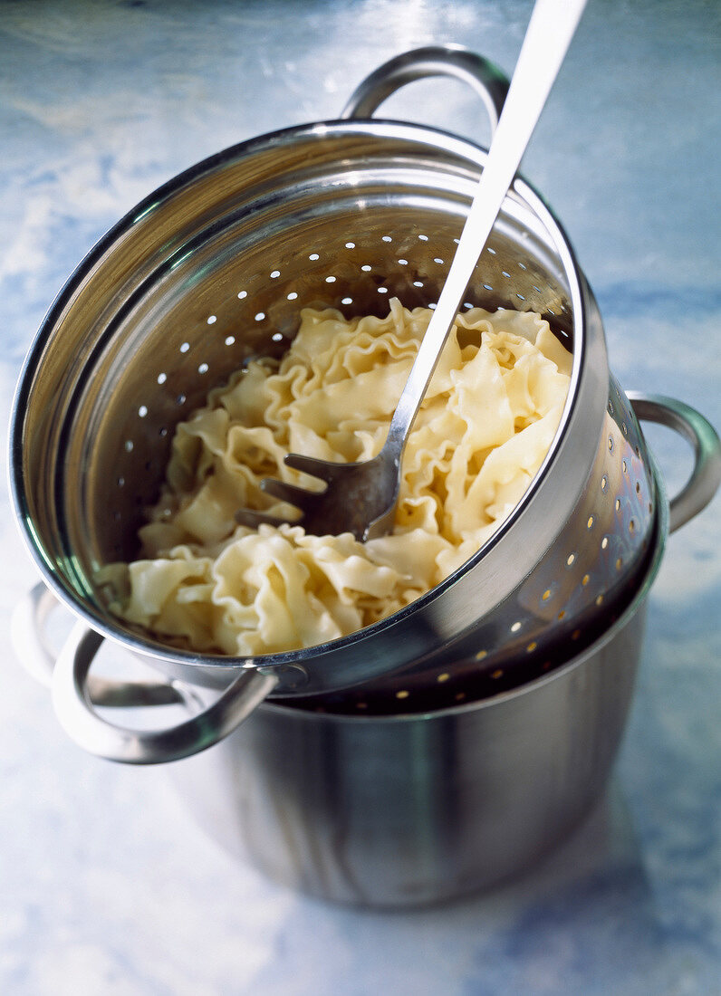 Gekochte Nudeln mit Pastalöffel in einem Abtropfsieb auf einem Edelstahltopf