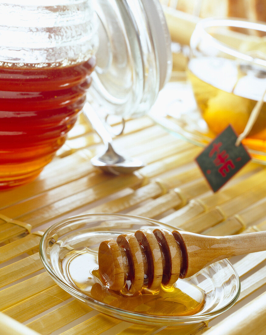 Honiglöffel neben Honigtopf, Teetasse im Hintergrund