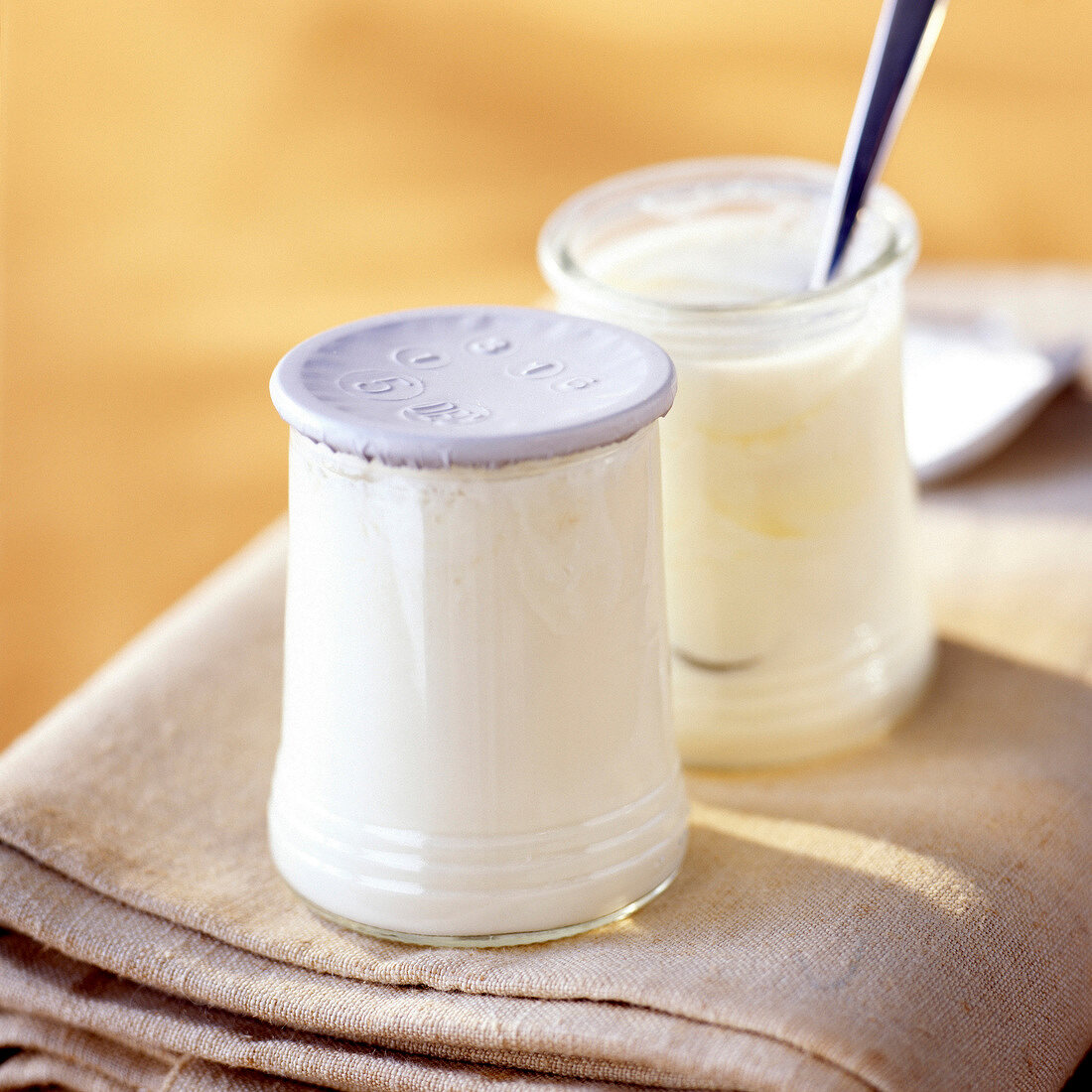 Zwei Gläser Naturjoghurt, eines geöffnet mit Löffel