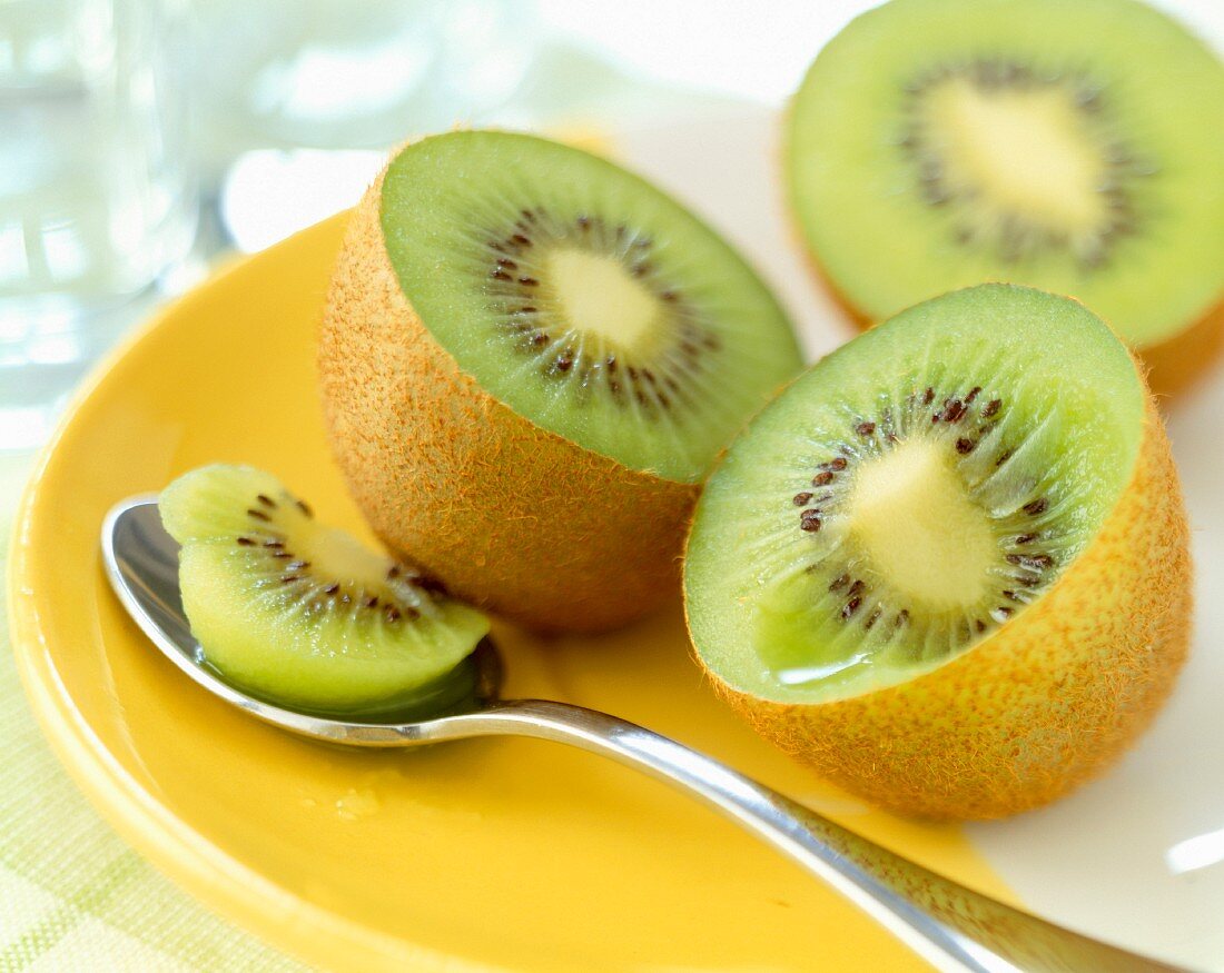 Halbierte mit Kiwi mit Löffel auf gelbem Teller