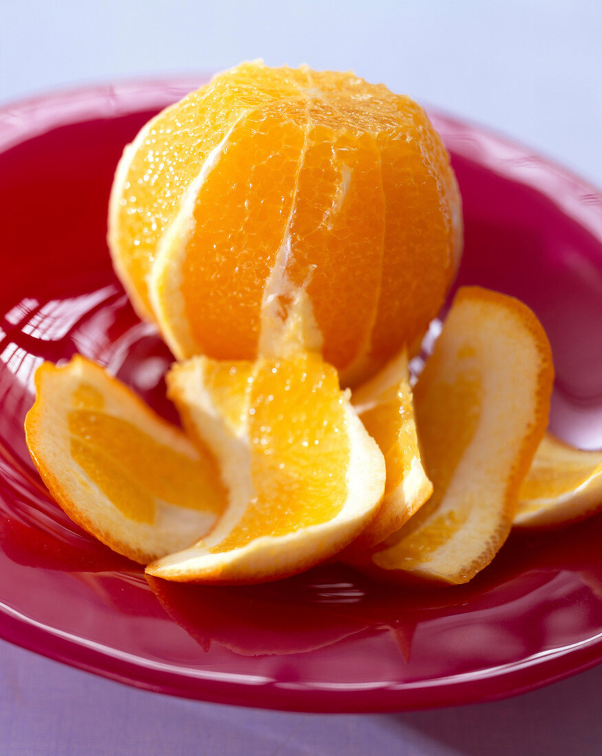 Geschälte Orange mit abgeschnittener Schale auf rotem Teller