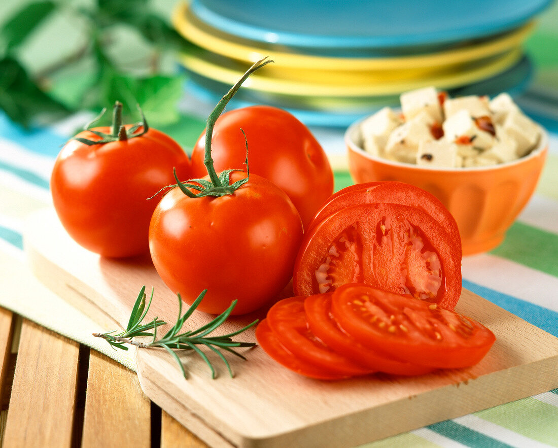 Whole and sliced tomatoes on chopping board