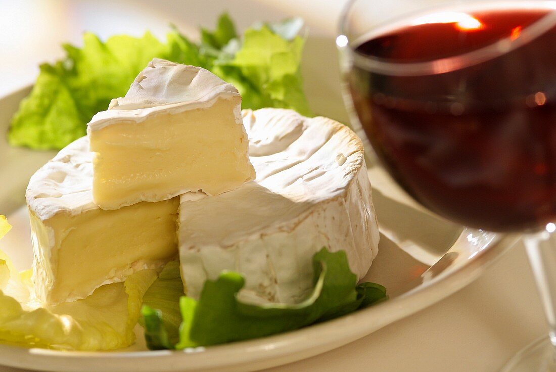 Angeschnittener Camembert mit Salatblättern und einem Glas Rotwein