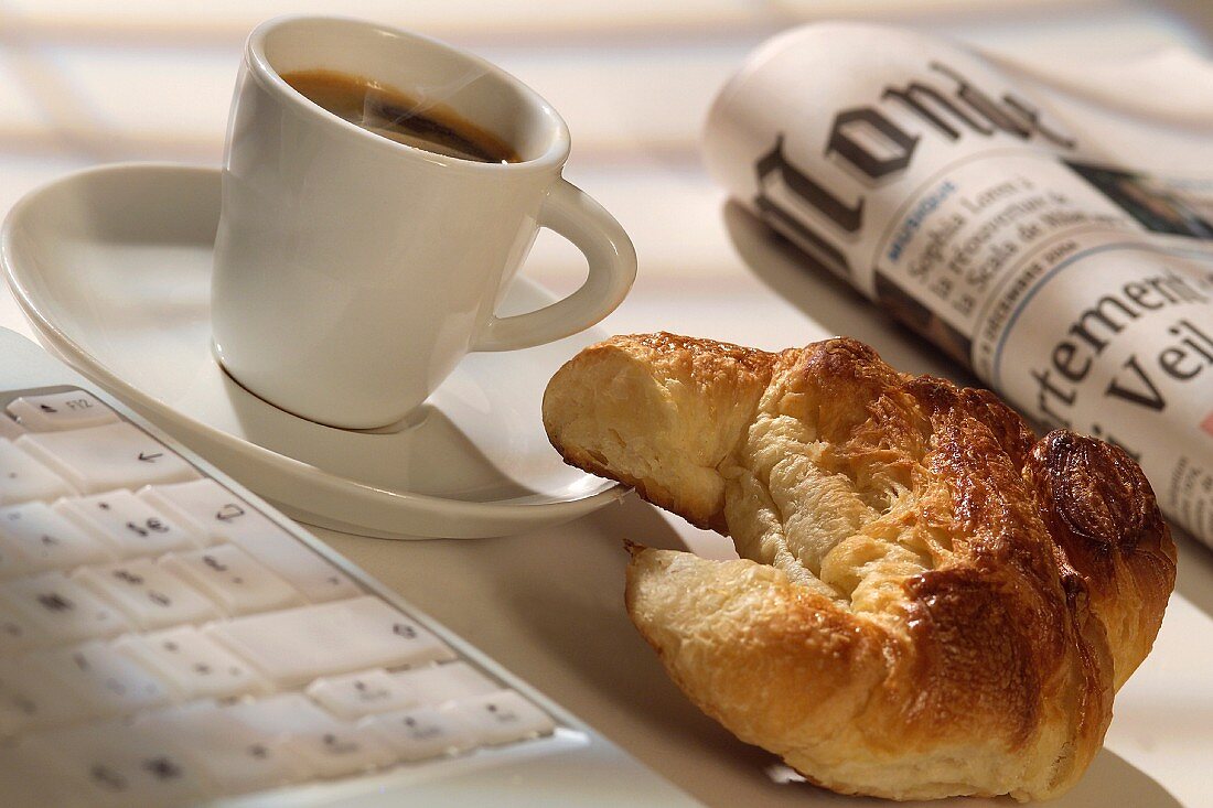 Ein Tasse Kaffee mit Croissant, französischer Zeitung und Laptop