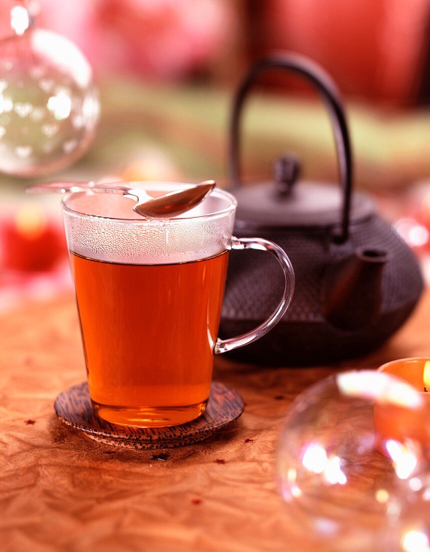 Eine Glastasse mit Tee und Teekanne im Hintergrund