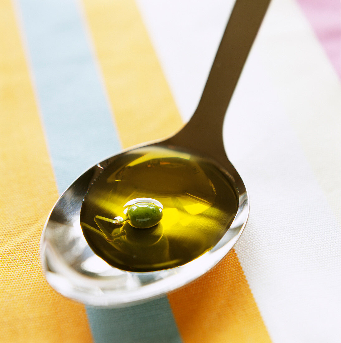 Olivenöl mit grüner Olive auf Löffel