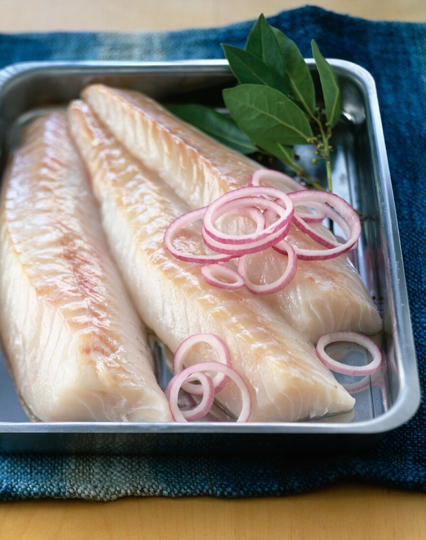 Kabeljaufilets mit Zwiebelringen und Lorbeerblättern auf tiefem Blech