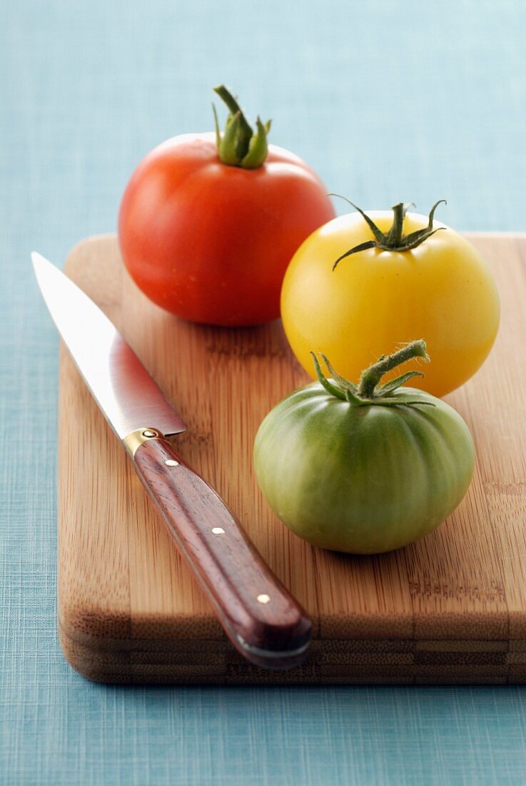 Three different coloured tomatoes on a chopping board