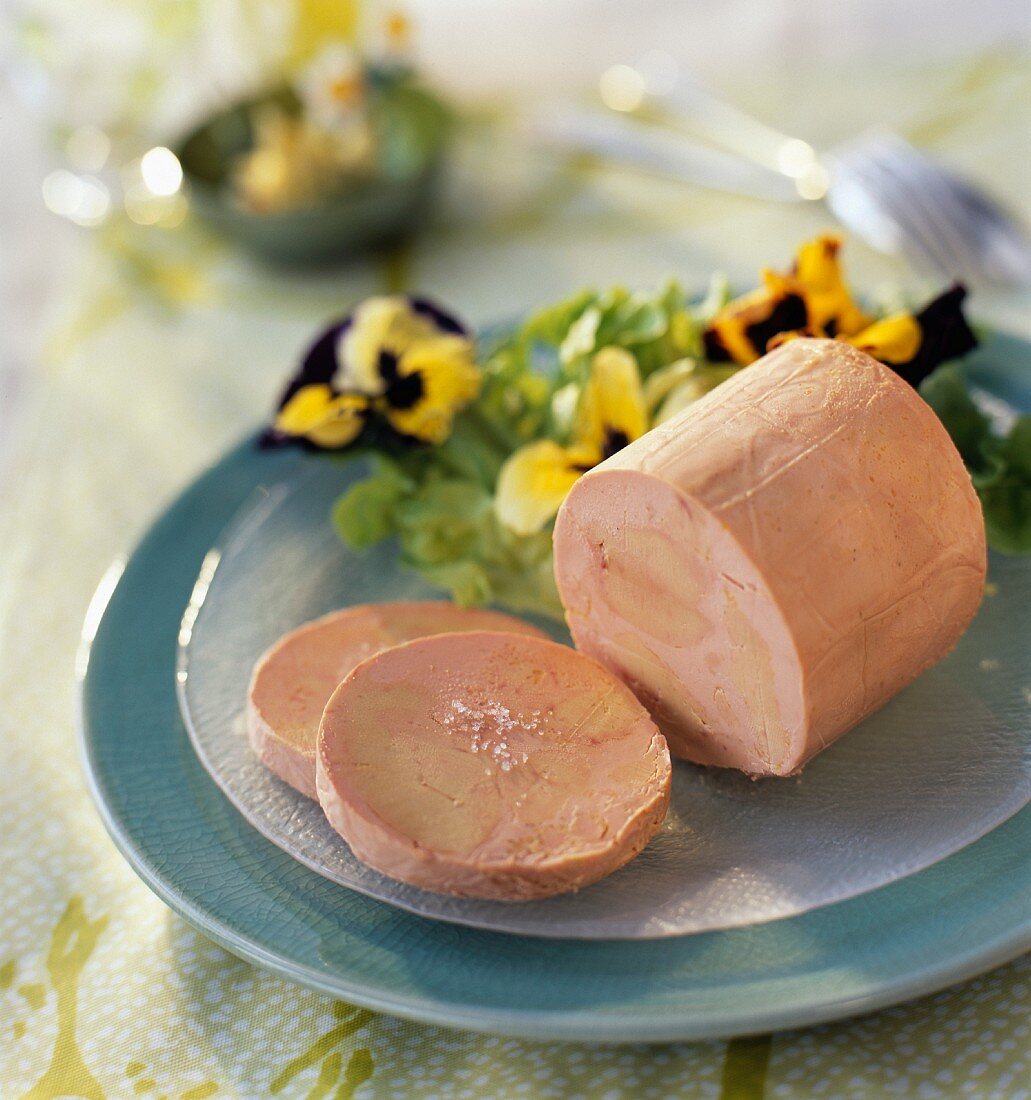Angeschnittener Gänseleberblock auf einem Teller mit Salat und Stiefmütterchenblüten