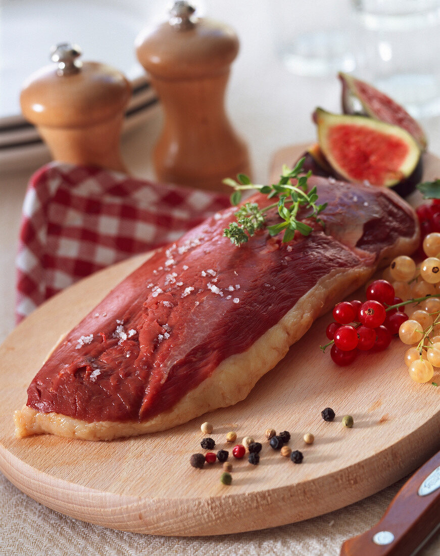 Rohe Entenbrust mit Gewürzen und Obst auf Holzbrett