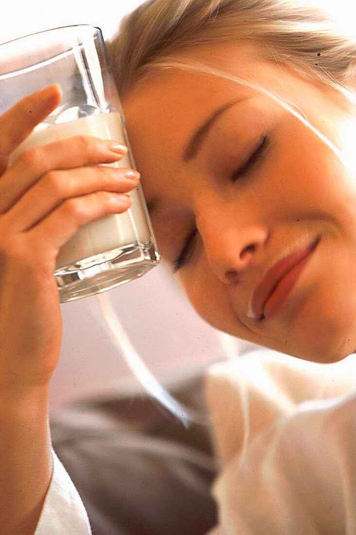 Frau mit geschlossenen Augen hält ein Glas Milch an die Stirn