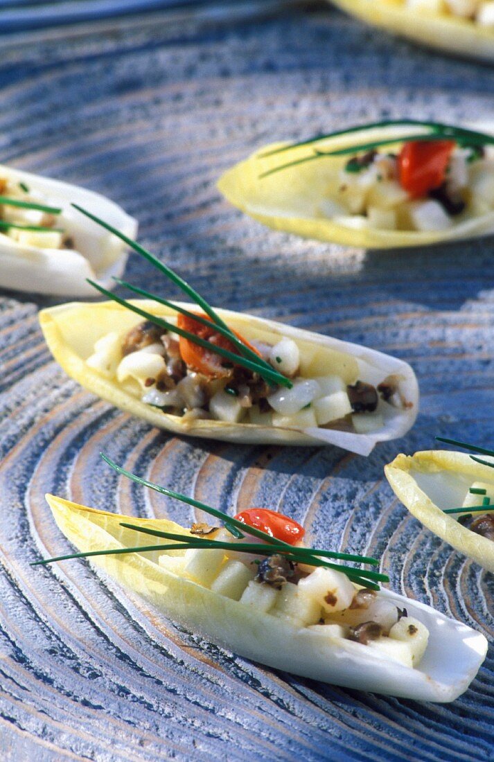 Chicoreeschiffchen mit Jakobsmuscheln, grünem Apfel und Schnittlauch auf blauem Untergrund