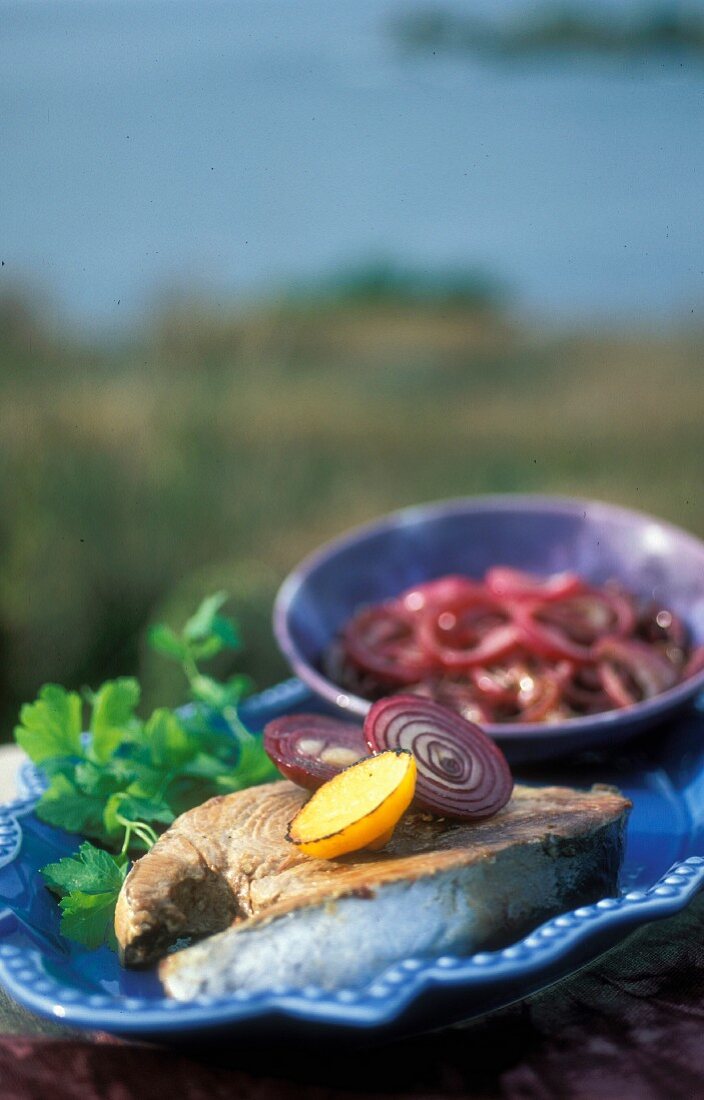 Thunfischsteak mit Zitrone, Petersilie und roter Zwiebel auf blauem Teller