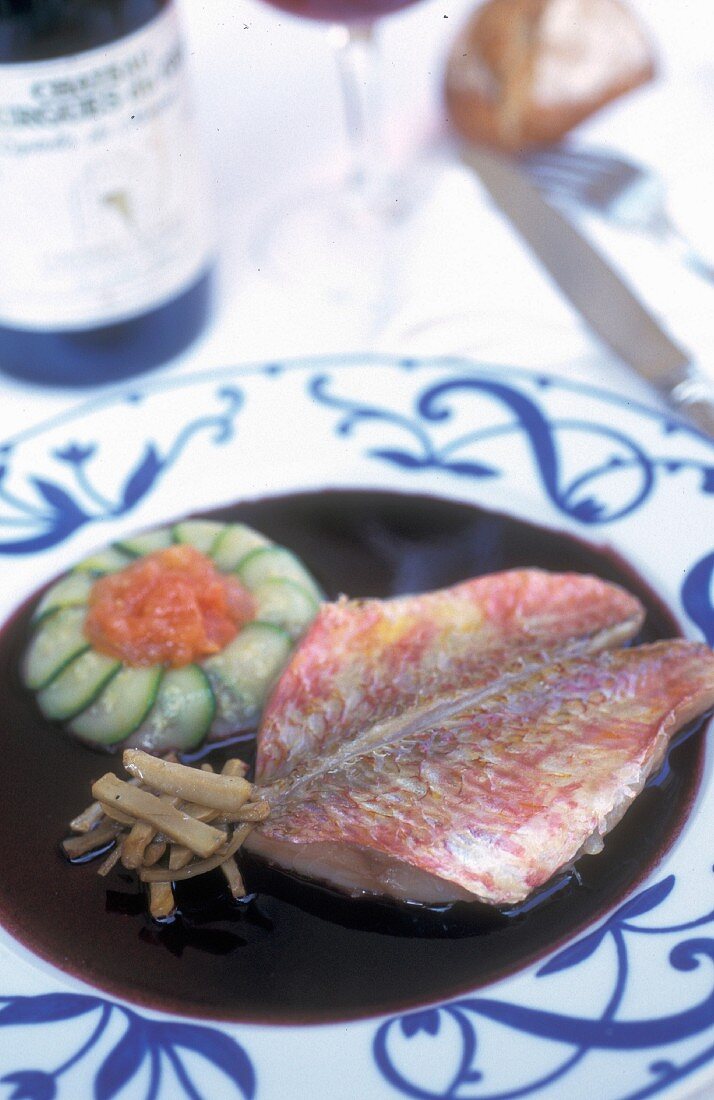 Provençal-style red mullet fillet in a red wine sauce on a white plate with an ornamental pattern