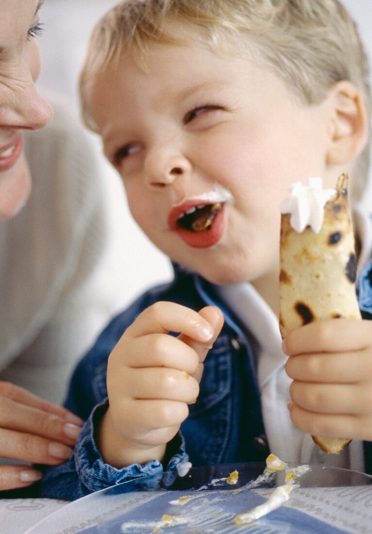 Kleiner Junge isst ein Crêpe mit Sahne