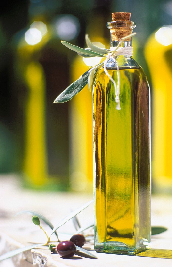 Flasche Olivenöl mit schwarzen Oliven und kleinen Olivenzweigen