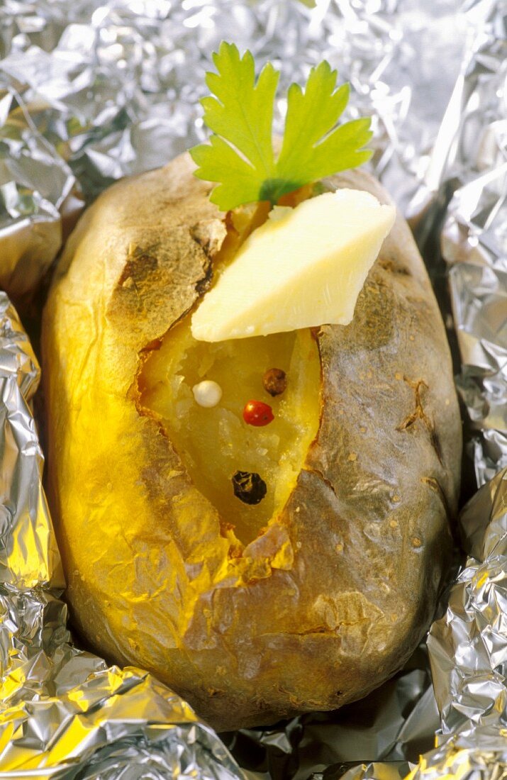 A baked potato with butter and pepper in aluminium foil