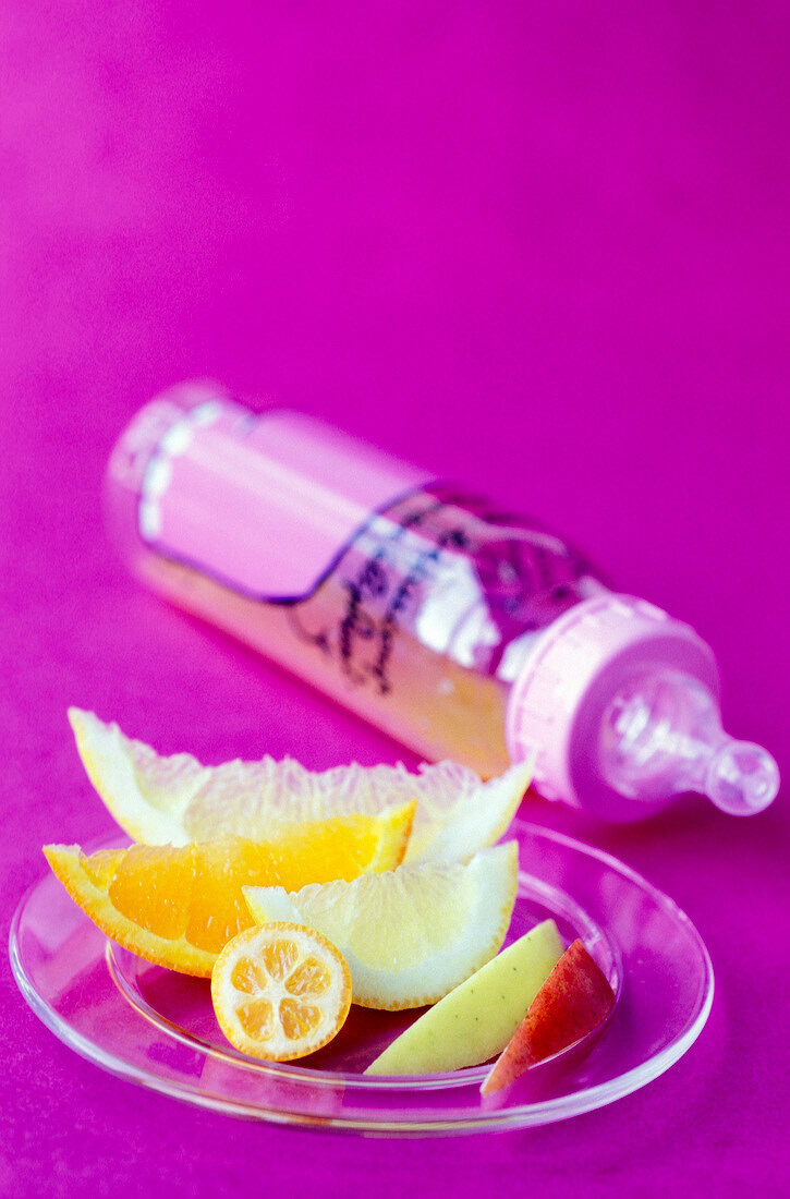 Frische Obststücke auf einem Teller, Babyflasche im Hintergrund