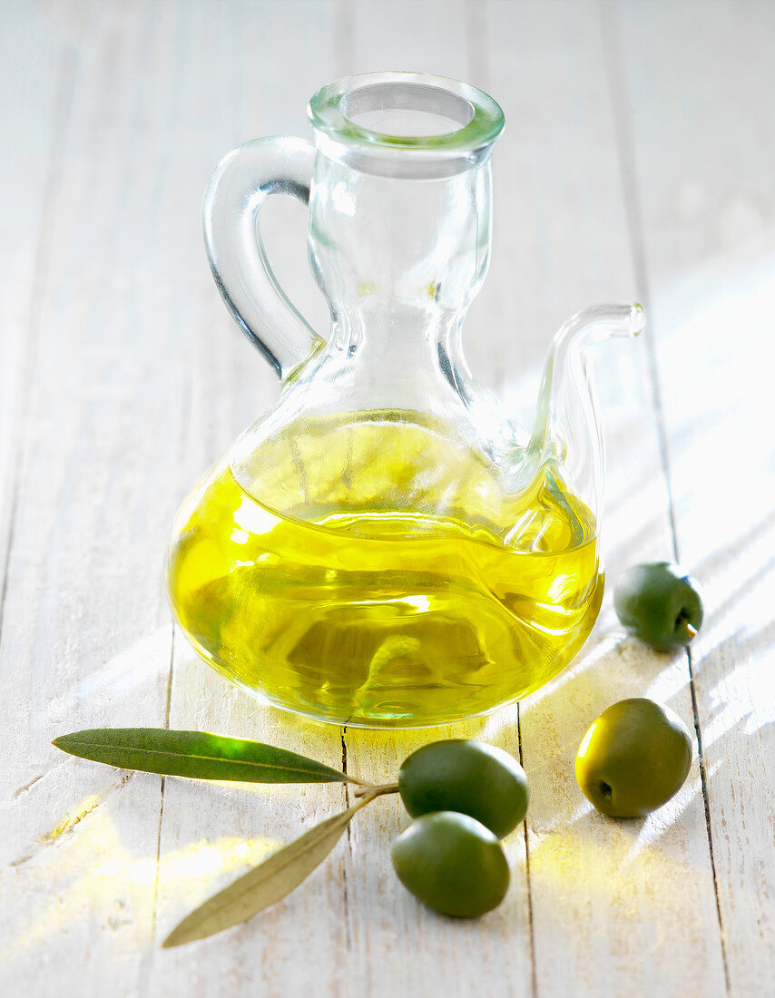 Flasche mit Olivenöl und grünen Oliven