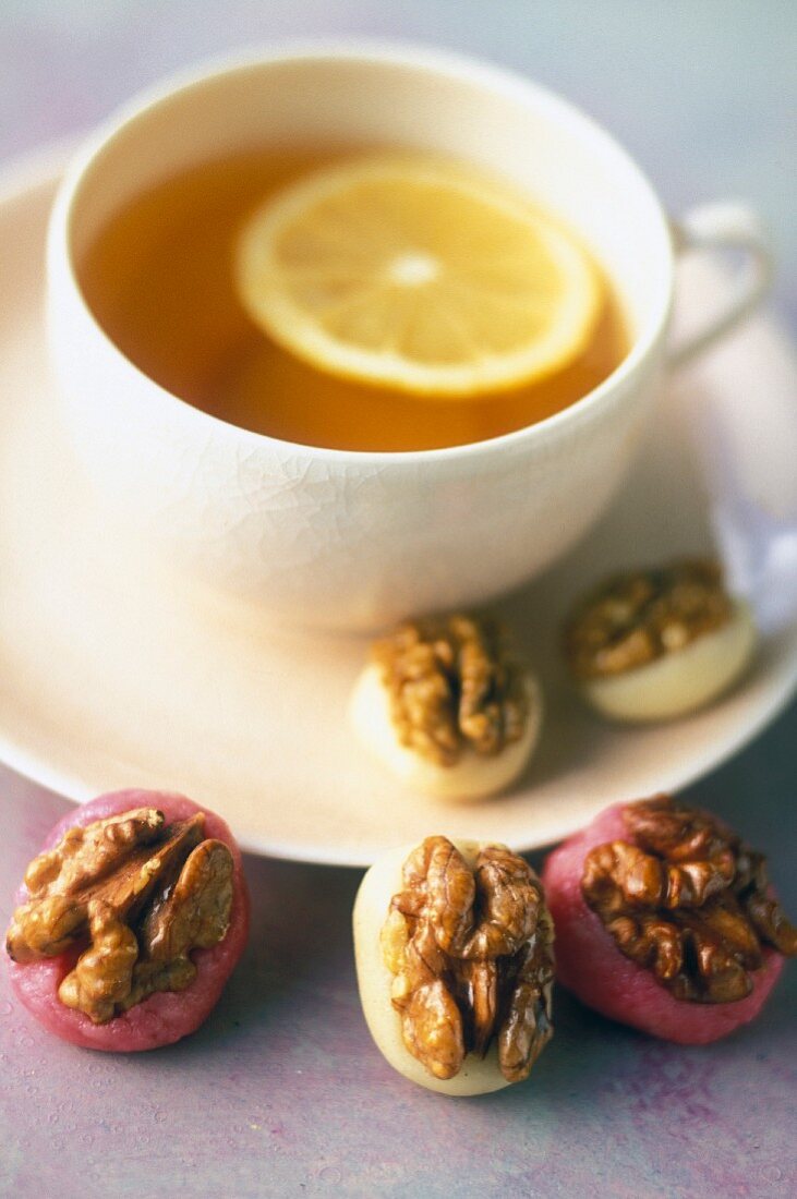 A cup of tea served with marzipan sweets with caramelised walnuts