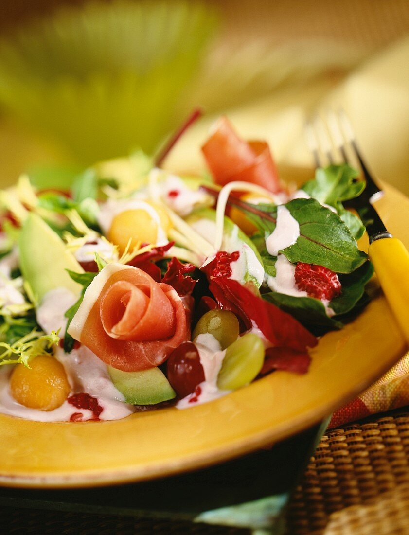 A mixed leaf salad with raw ham and fresh fruits
