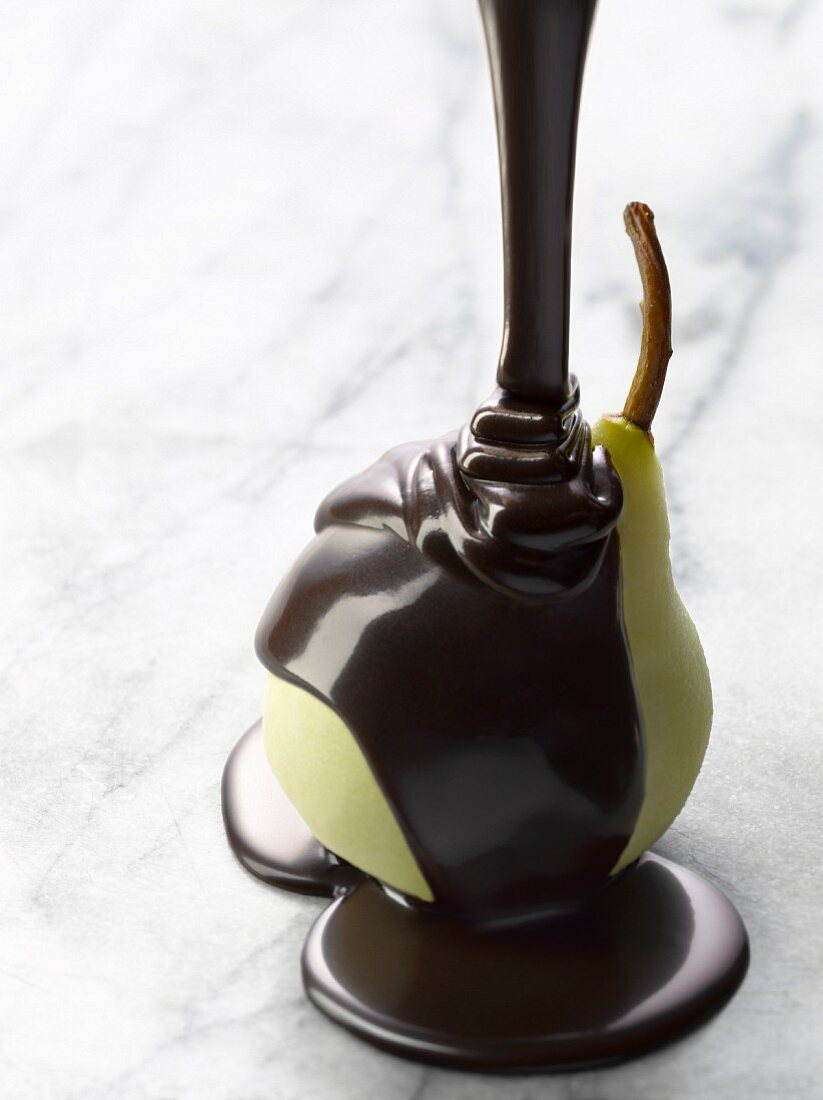 Pouring melted chocolate onto a peeled pear