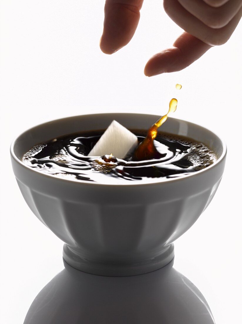 Zucker in eine Schüssel mit schwarzem Kaffee geben