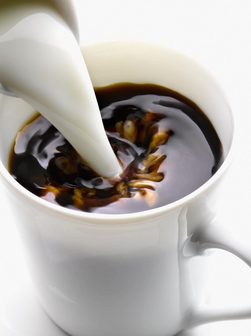 Milch wird eine Tasse schwarzen Kaffee gegossen