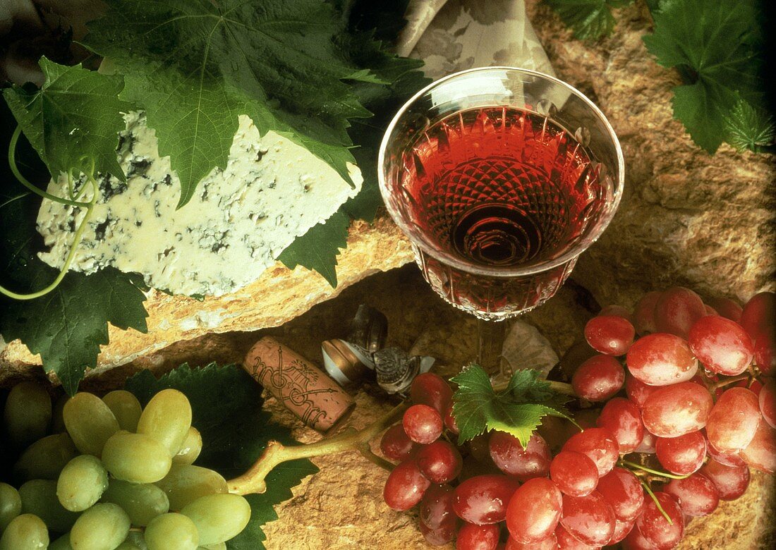 Stillleben mit Glas Rotwein neben Trauben und Blauschimmelkäse