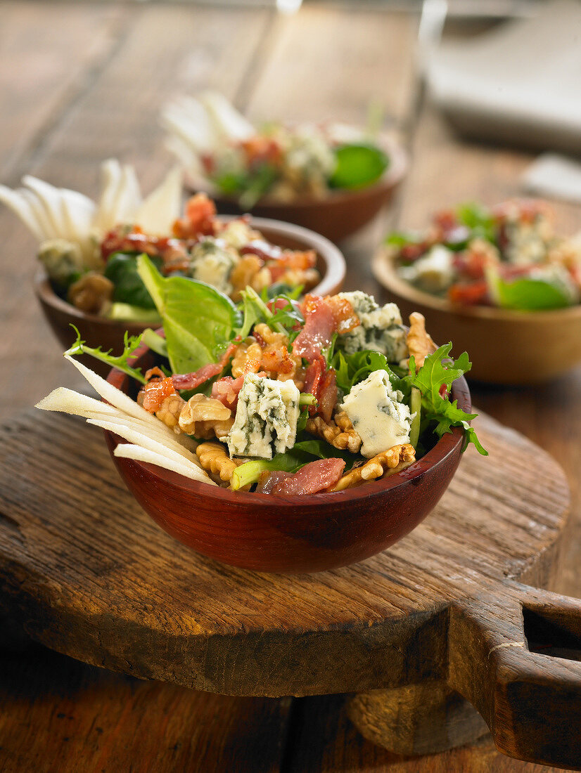 Herbstlicher Salat mit Spinat, Käse, Birnen, Speck und Nüssen serviert mit Honigdressing