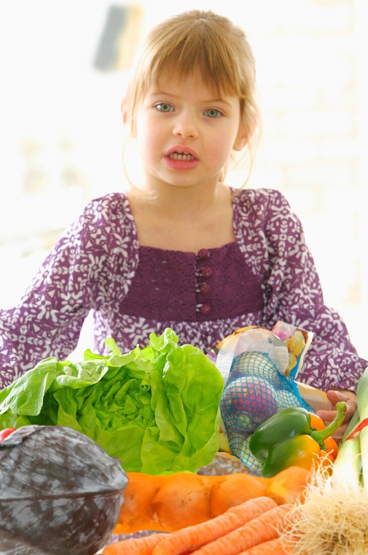 Kleines Mädchen steht hinter einem Tisch mit Gemüse